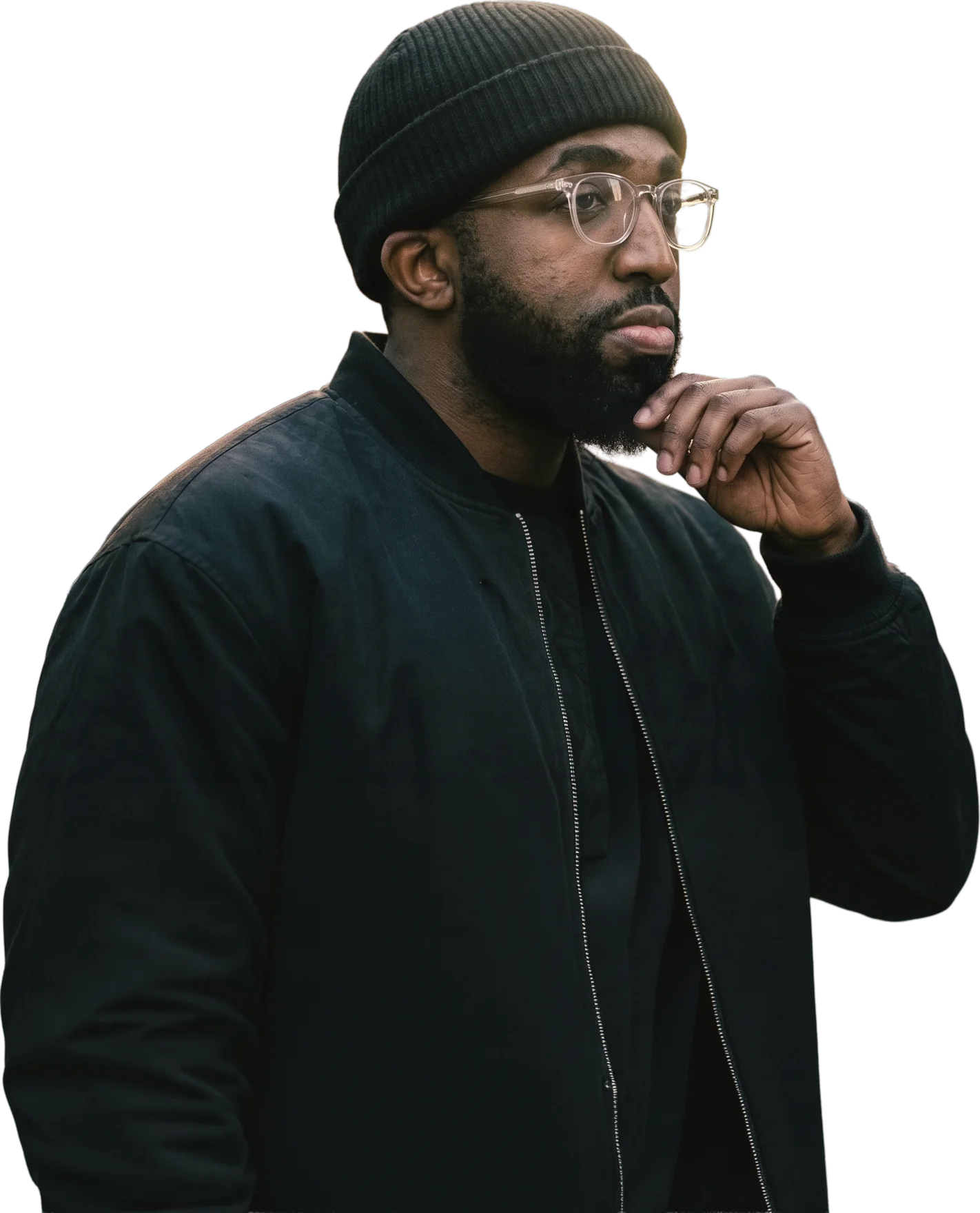 Christen Brown, known as Ten, in a black beanie, clear glasses and bomber jacket, hand on chin